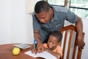 Dad Helps His Child To Write At Home.